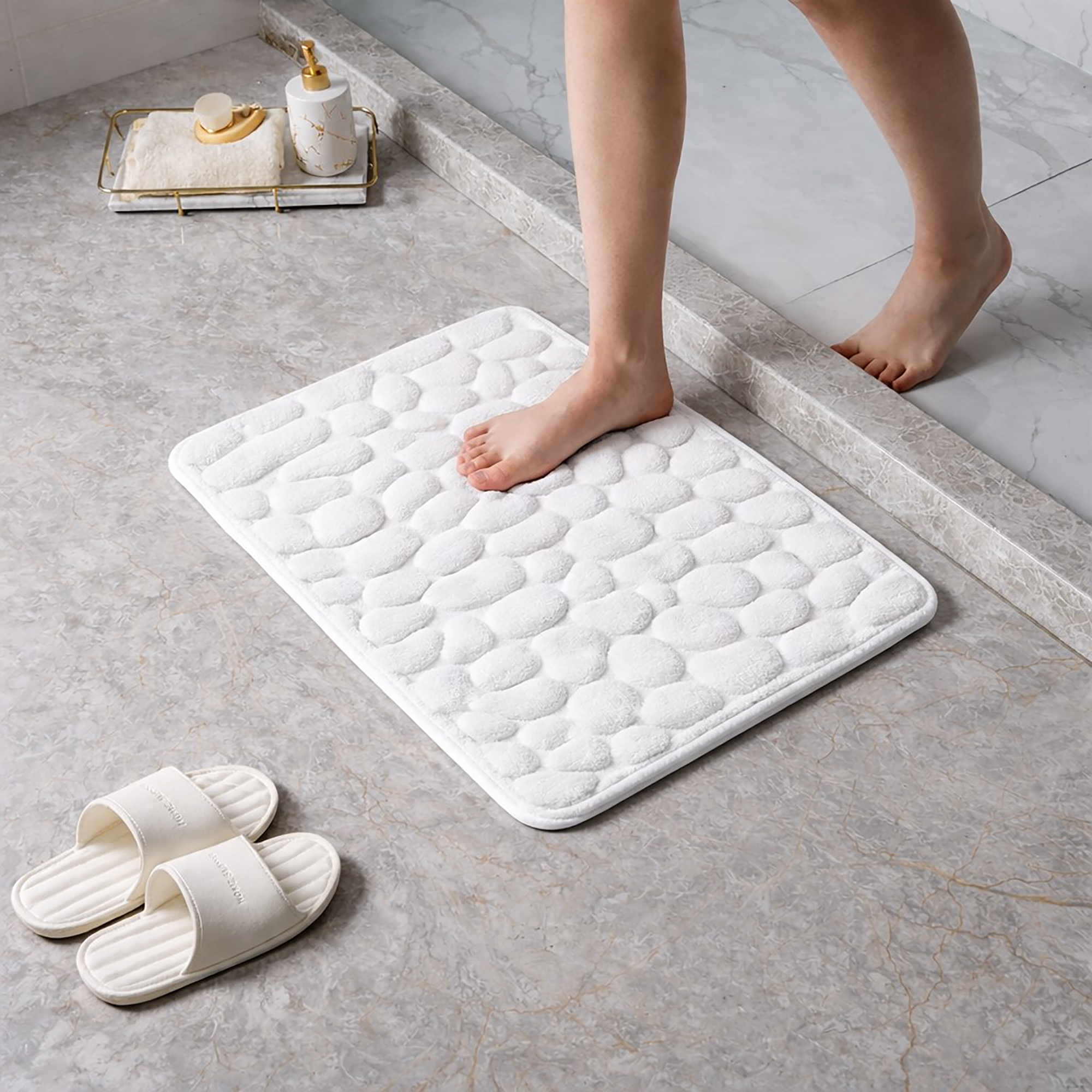 Barefoot stepping on a soft white pebble design memory foam mat placed on a bathroom tile floor