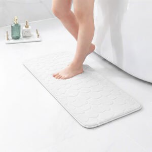 Barefoot stepping on a long white runner mat with pebble texture placed on a bathroom tile floor next to a tub
