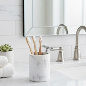 White marble bathroom tumbler with toothbrushes and razor on vanity