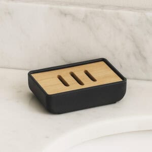 Black rubber soap dish with bamboo slotted tray shown empty on marble surface