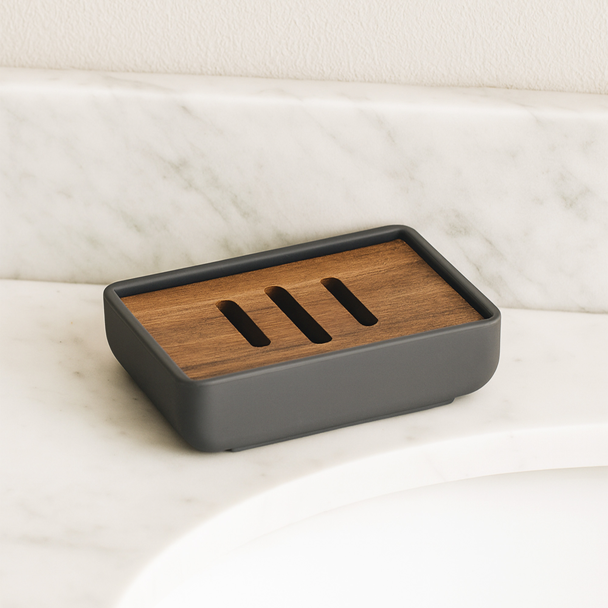 Empty gray soap dish with acacia wood slotted insert on marble countertop