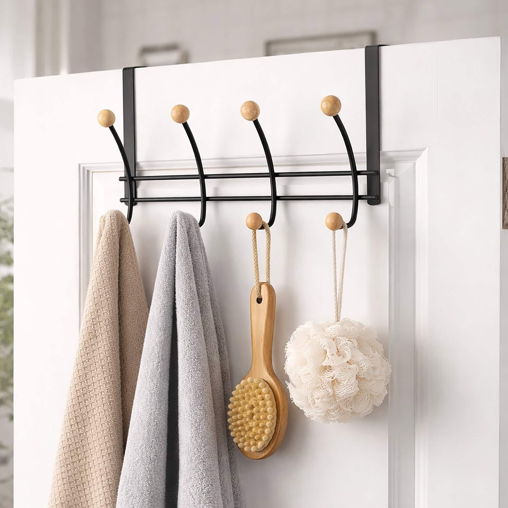"Black over-the-door hook rack with wood ball ends holding towels, bath brush, and loofah on white door"