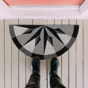 Outdoor view of half-round compass rose coir doormat placed at front doorstep on wood planks