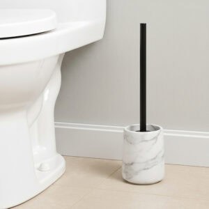 White marble toilet brush holder with black handle next to white toilet
