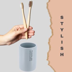 Hand holding two bamboo toothbrushes above soft blue tumbler cup