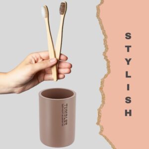 Hand holding two bamboo toothbrushes above soft blue tumbler cup