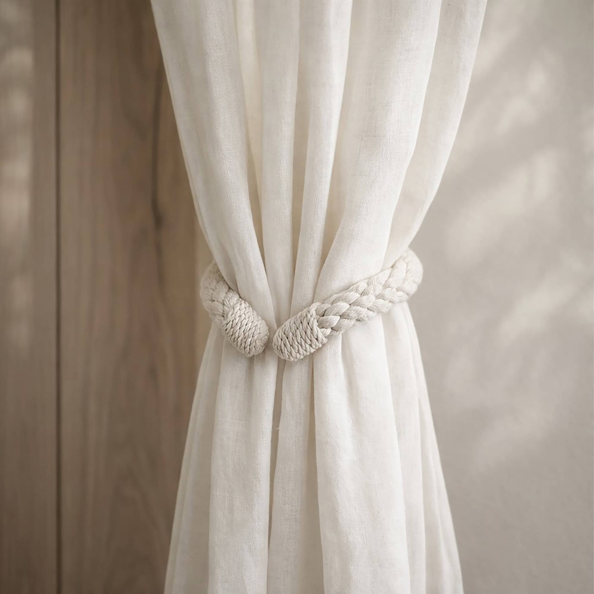 "Cotton rope tieback holding a gathered sheer curtain against a wood-toned wall"