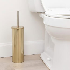 Brushed gold toilet brush with stainless steel handle in cylindrical holder beside white toilet