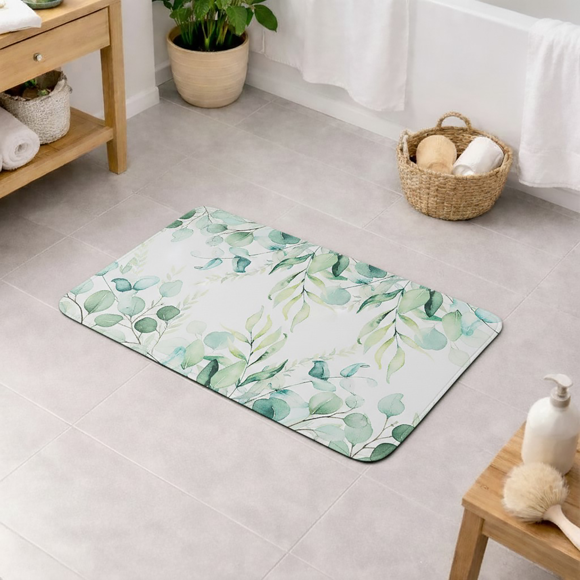 White bath mat with watercolor eucalyptus leaves border pattern on a bathroom floor, surrounded by a wooden shelf, woven basket with bath accessories, bathtub, and soap dispenser with brush.