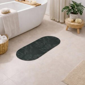 Oval runner bath mat with dark green tropical palm leaf pattern on a bathroom floor next to a freestanding tub, woven stool with plant, wicker basket with towels, and jute rug.