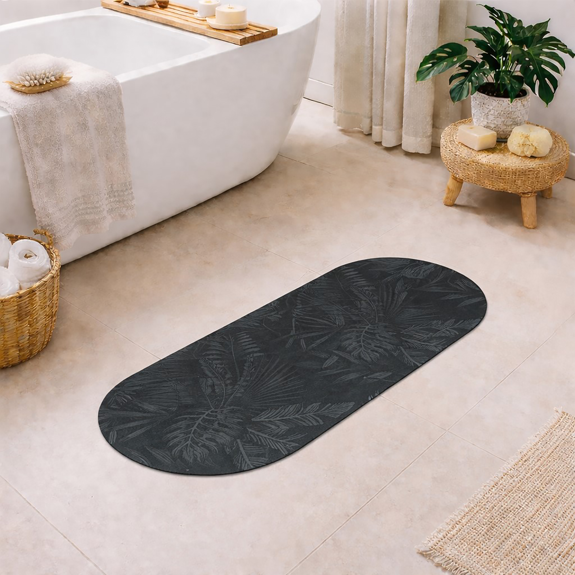 Oval runner bath mat with dark green tropical palm leaf pattern on a bathroom floor next to a freestanding tub, woven stool with plant, wicker basket with towels, and jute rug.