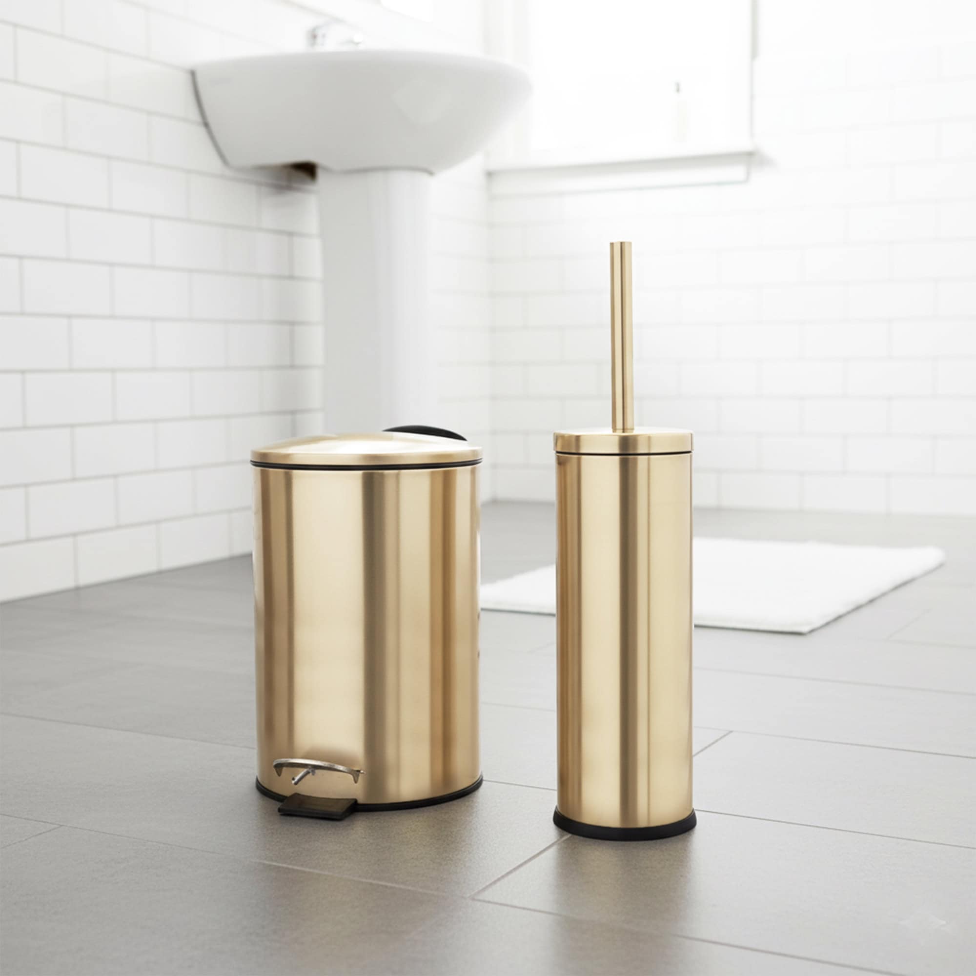 Gold trash can and toilet brush set on gray tile in white bathroom