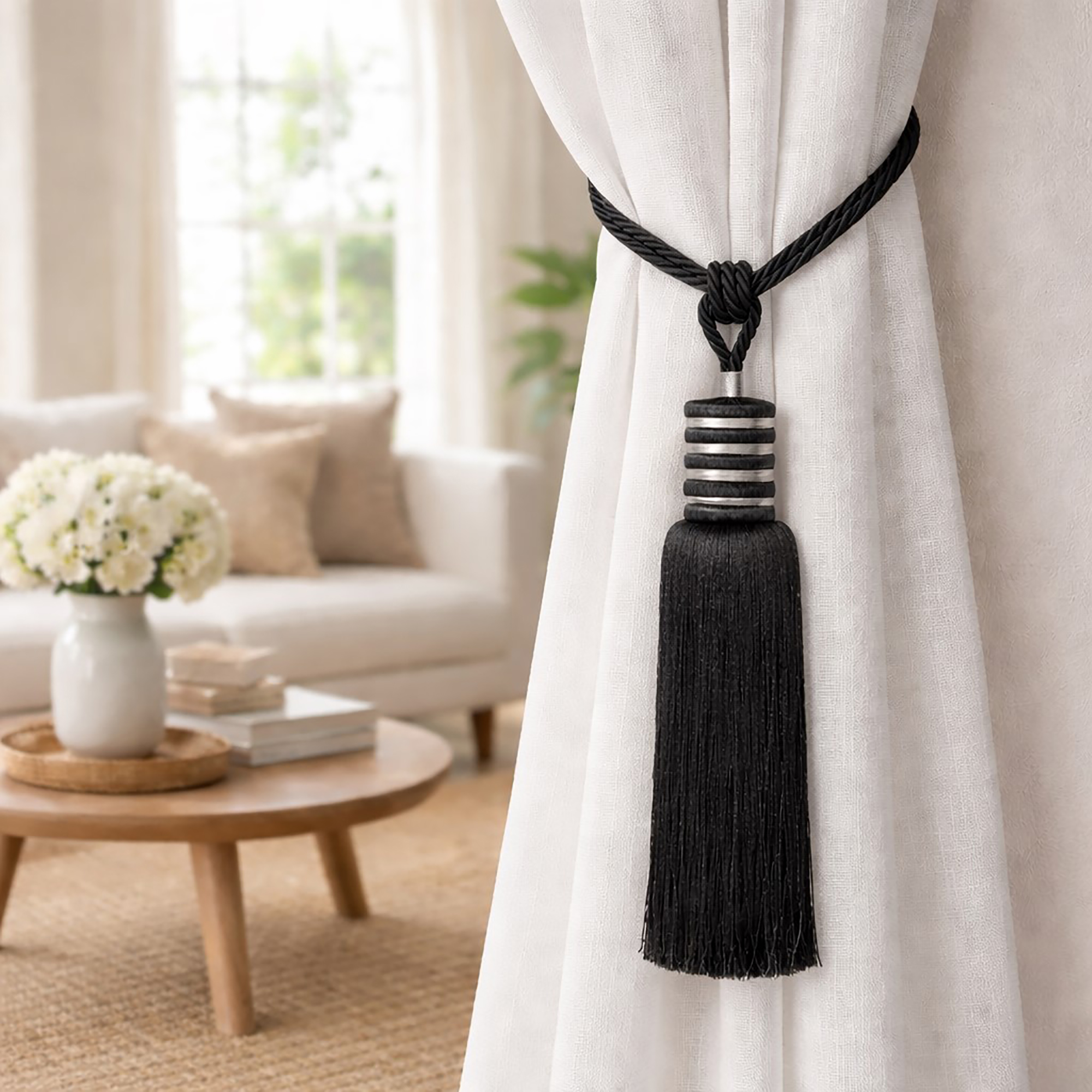 Close-up of a midnight black curtain tieback with twisted rope loop and tassel holding a white sheer curtain
