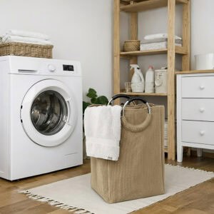 Sand beige corduroy laundry basket with silver metal handles holding white towels, placed next to a front-load washing machine in an organized laundry room.