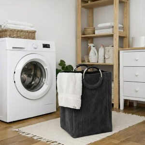 Charcoal gray corduroy laundry basket with silver metal handles holding white towels, placed next to a front-load washing machine in an organized laundry room.