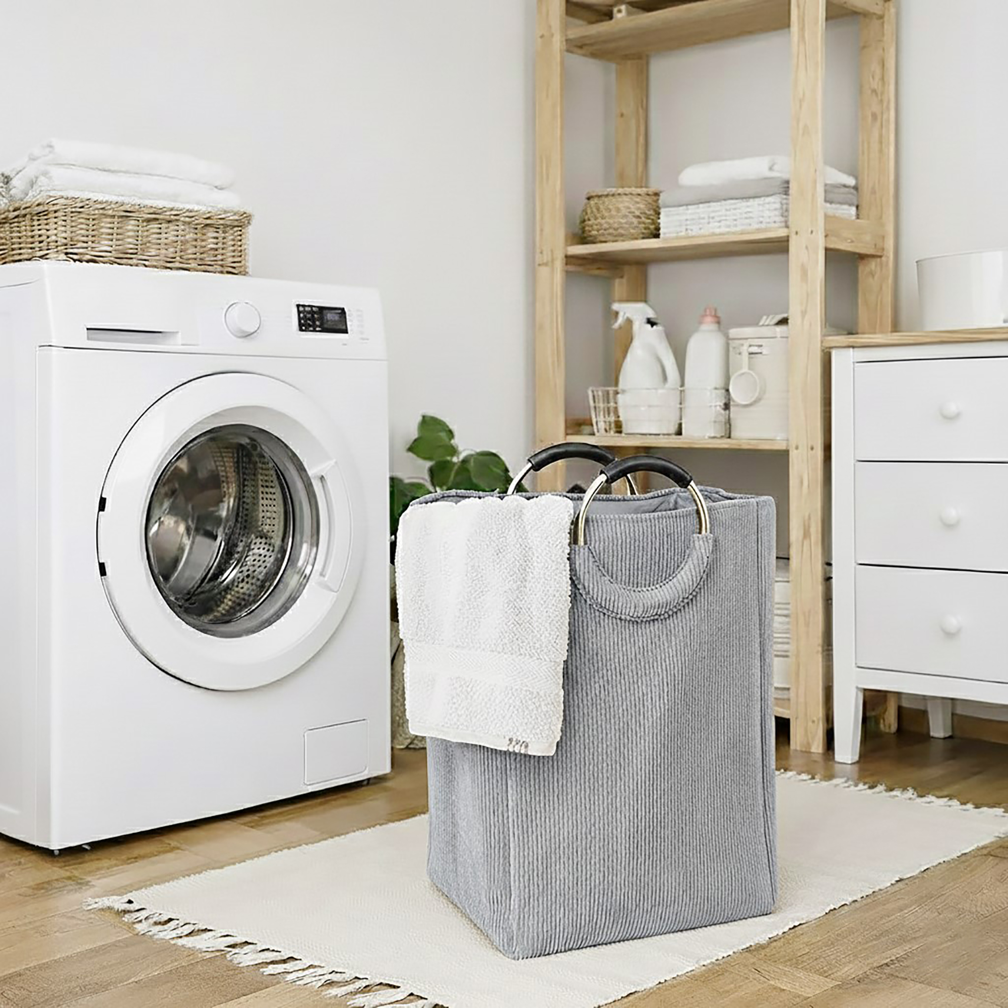 Soft gray corduroy laundry basket with silver metal handles holding white towels, placed next to a front-load washing machine in an organized laundry room.