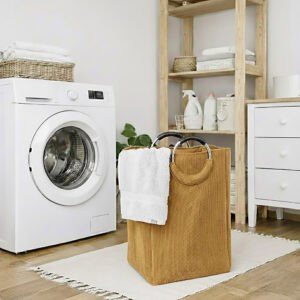 Mustard yellow corduroy laundry basket with silver metal handles holding white towels, placed next to a front-load washing machine in an organized laundry room.