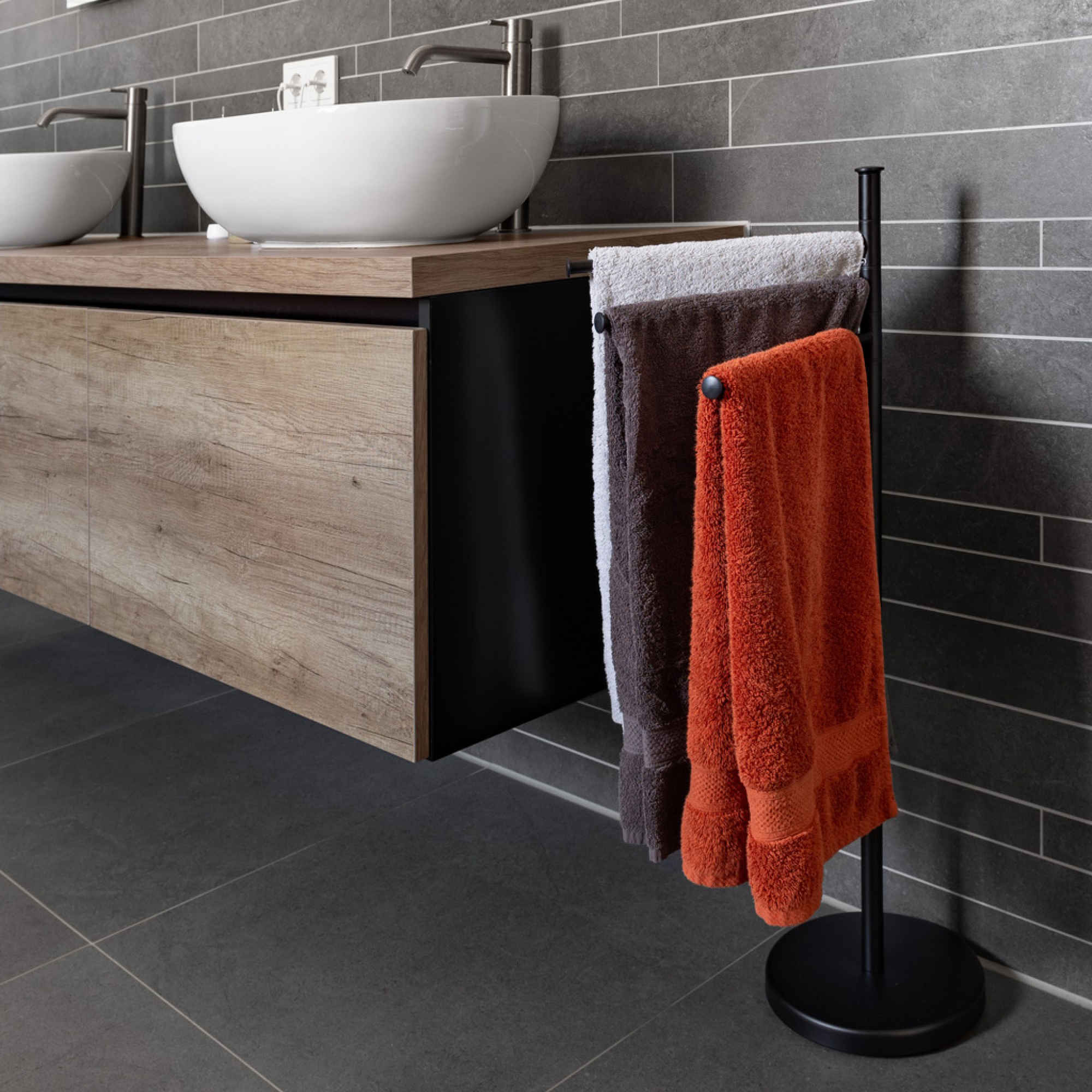 Black towel rack holding three towels beside a modern wood vanity