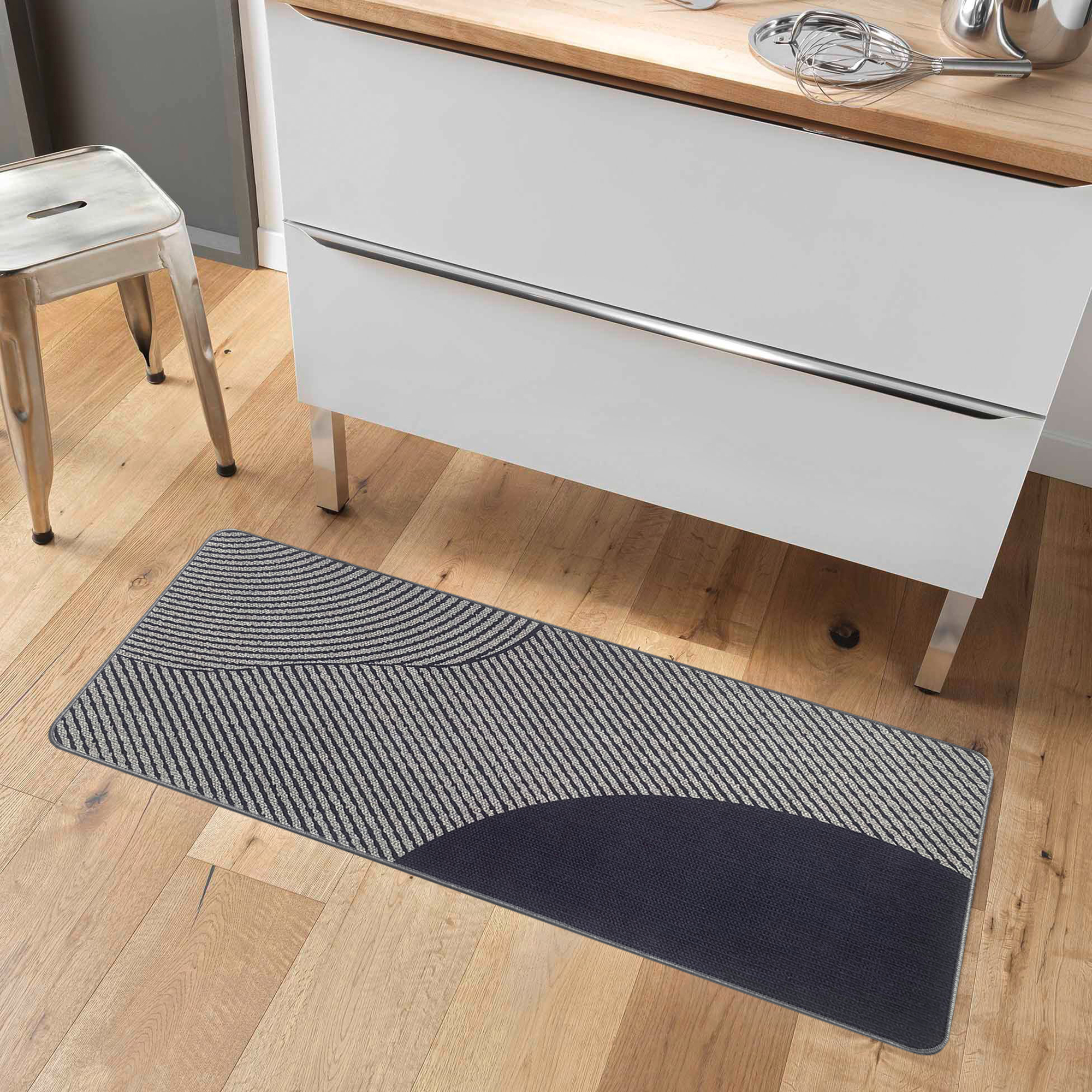 Kitchen runner mat placed on wood floor beside white cabinets with a modern metal stool