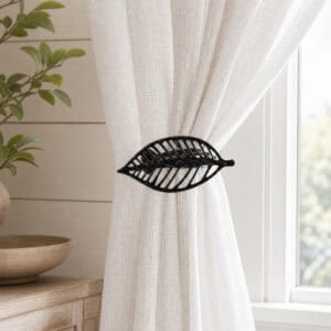 Textured black leaf curtain tieback holding back a white linen sheer panel by a window