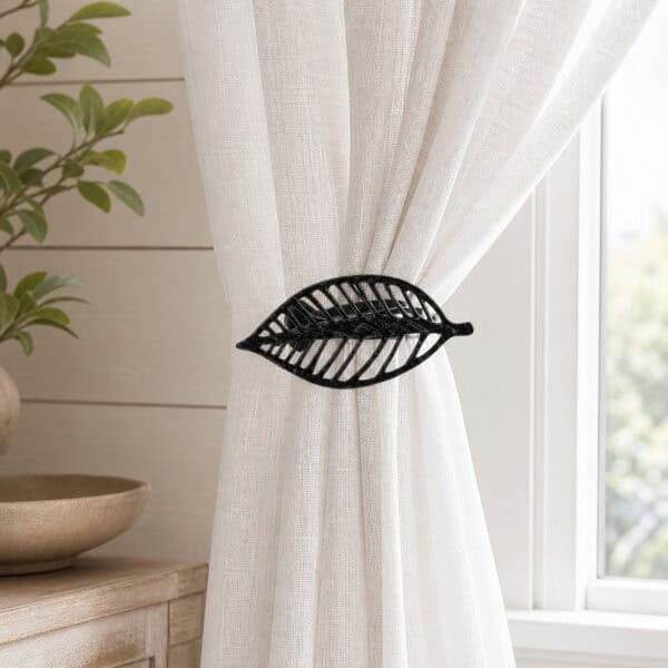 Textured black leaf curtain tieback holding back a white linen sheer panel by a window
