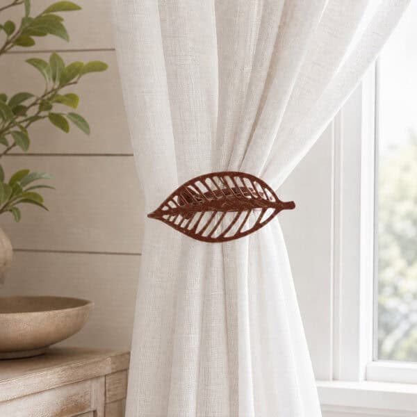 Rustic brown leaf curtain tieback holding back a white linen sheer panel by a window
