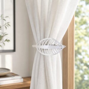 Polished silver leaf curtain tieback holding back a white sheer panel against a wood frame