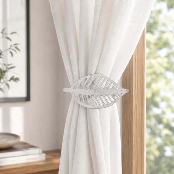 Whitewash leaf curtain tieback holding back a white sheer panel against a wood frame