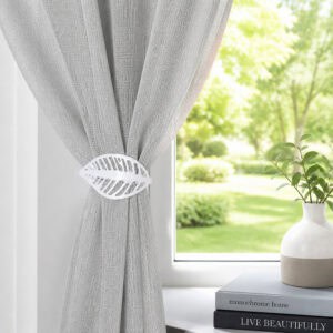 Polished silver leaf curtain tieback on a gray sheer panel by a sunny window with a vase