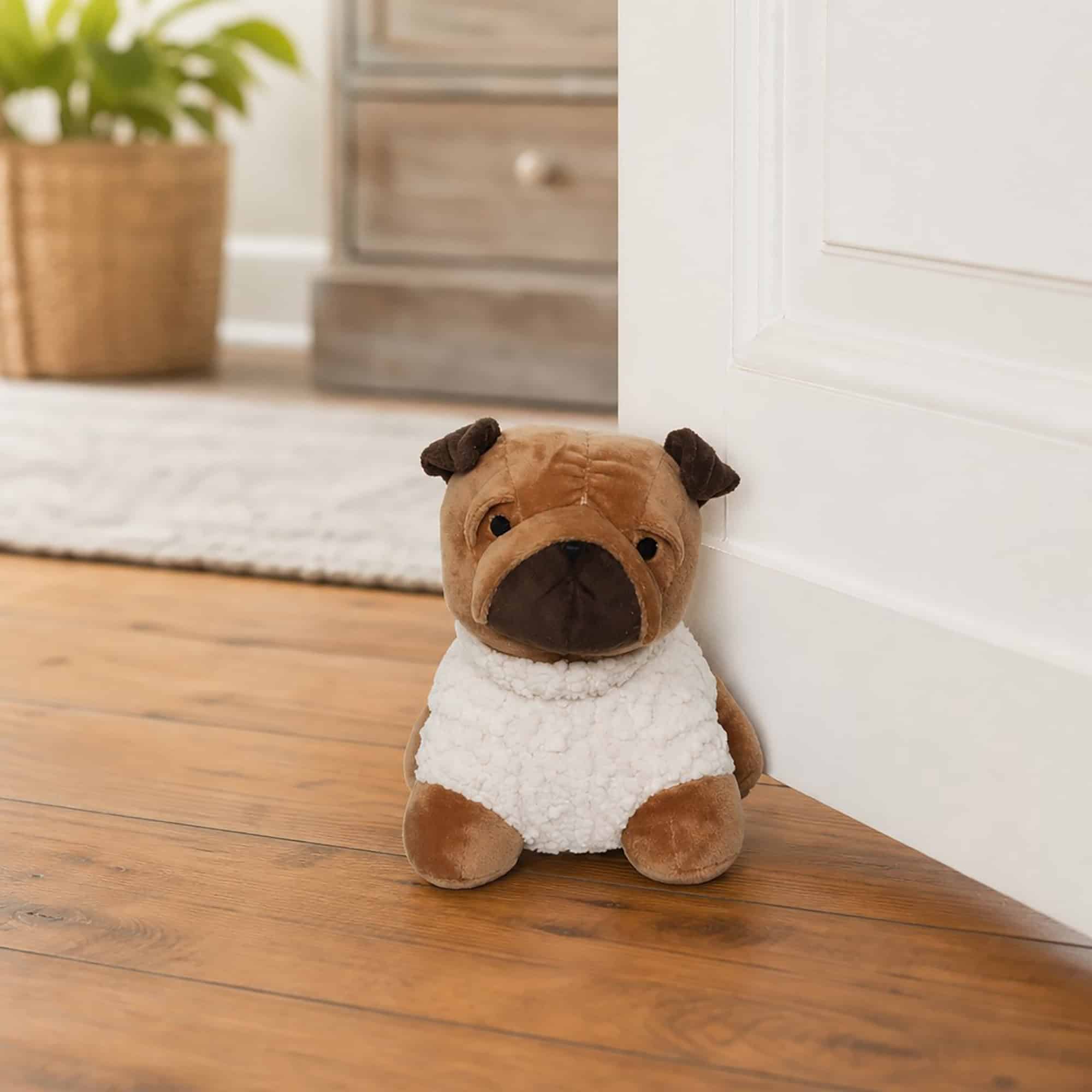 Tan pug door stopper propping open a white paneled door on hardwood floor, wooden dresser and plant in the background.