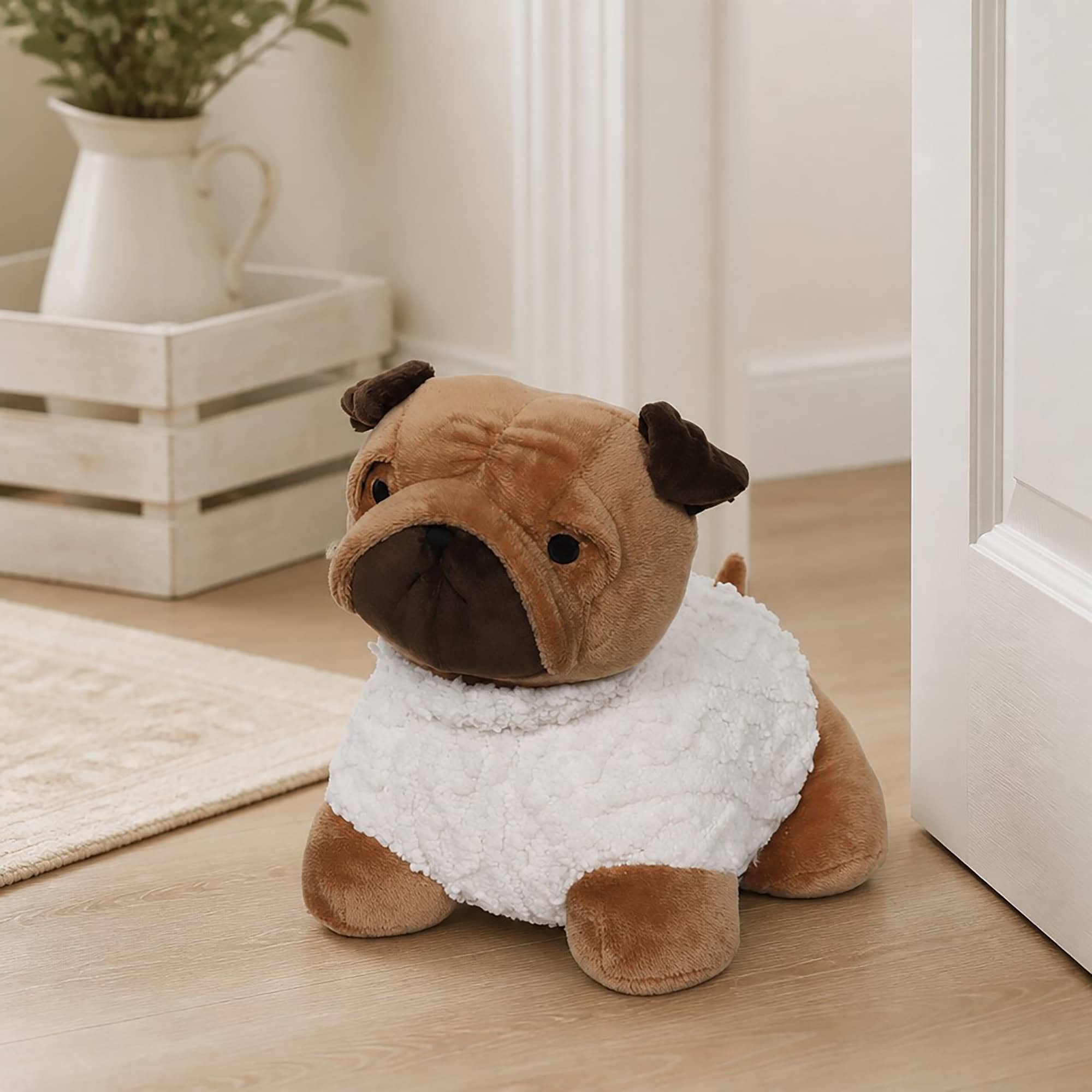 Tan pug door stopper propping open a white door on hardwood floor, wooden crate with a pitcher and plant in the background.