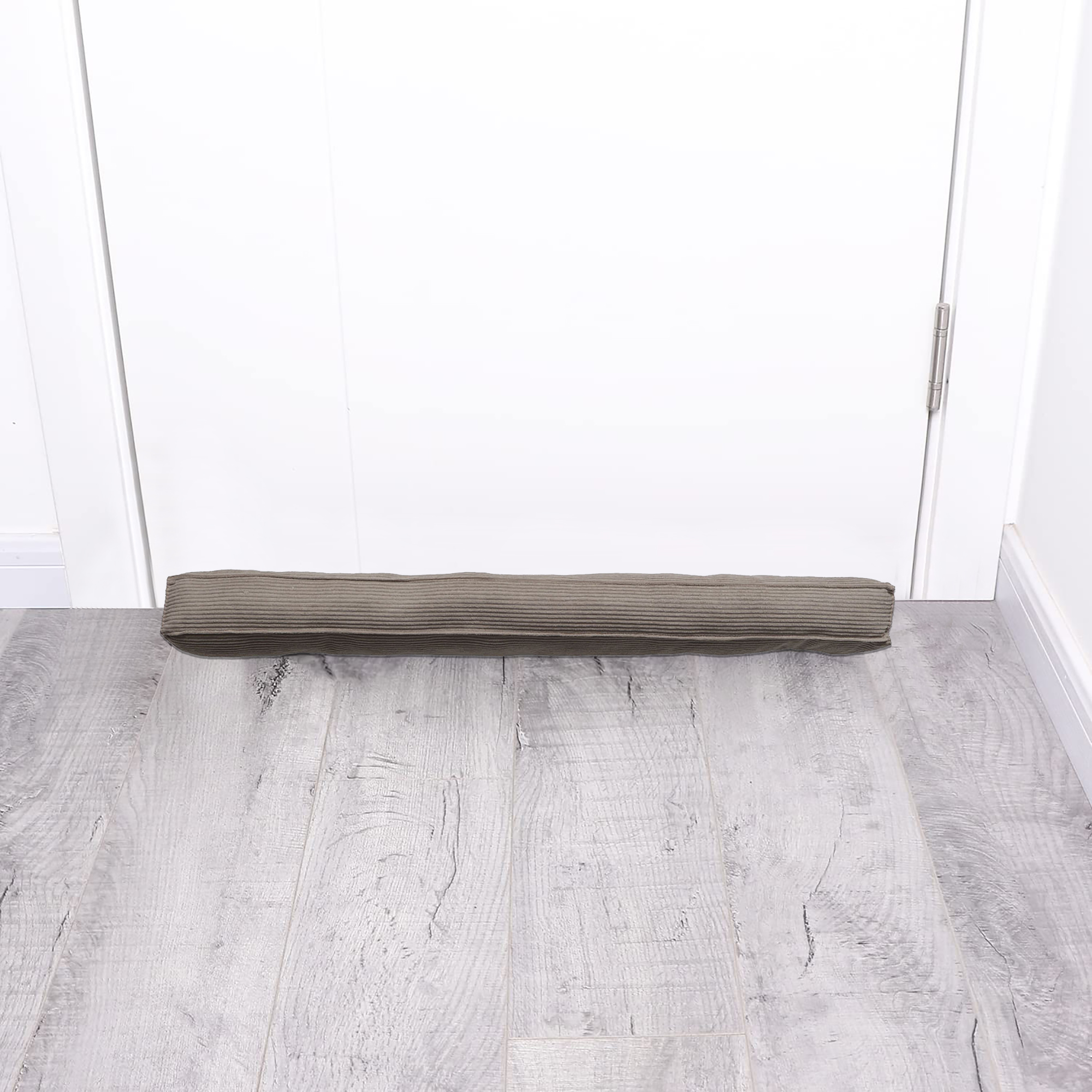Corduroy draft stopper placed at the bottom of a closed white door on gray wood floor