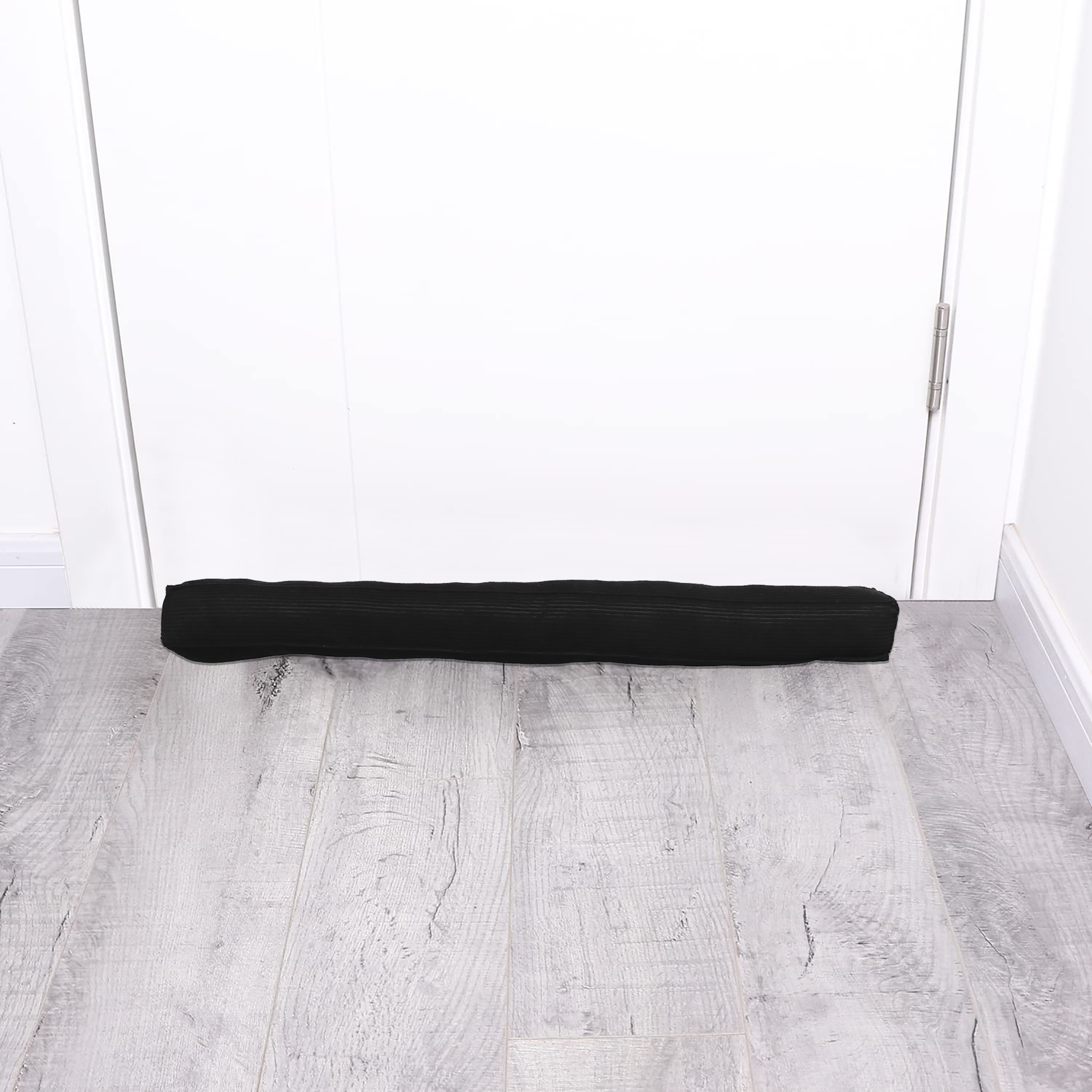 Corduroy draft stopper placed at the bottom of a closed white door on gray wood floor