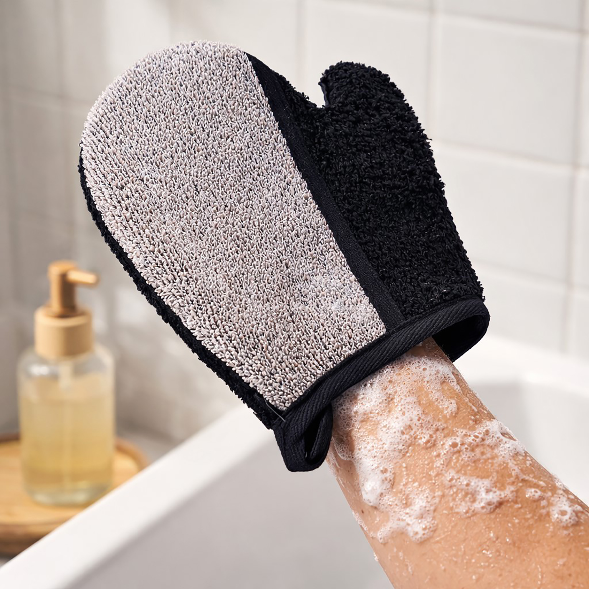 Person wearing exfoliating glove on soapy arm in bathroom