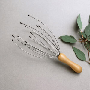 Head massager styled on white surface with green eucalyptus leaves for natural spa aesthetic