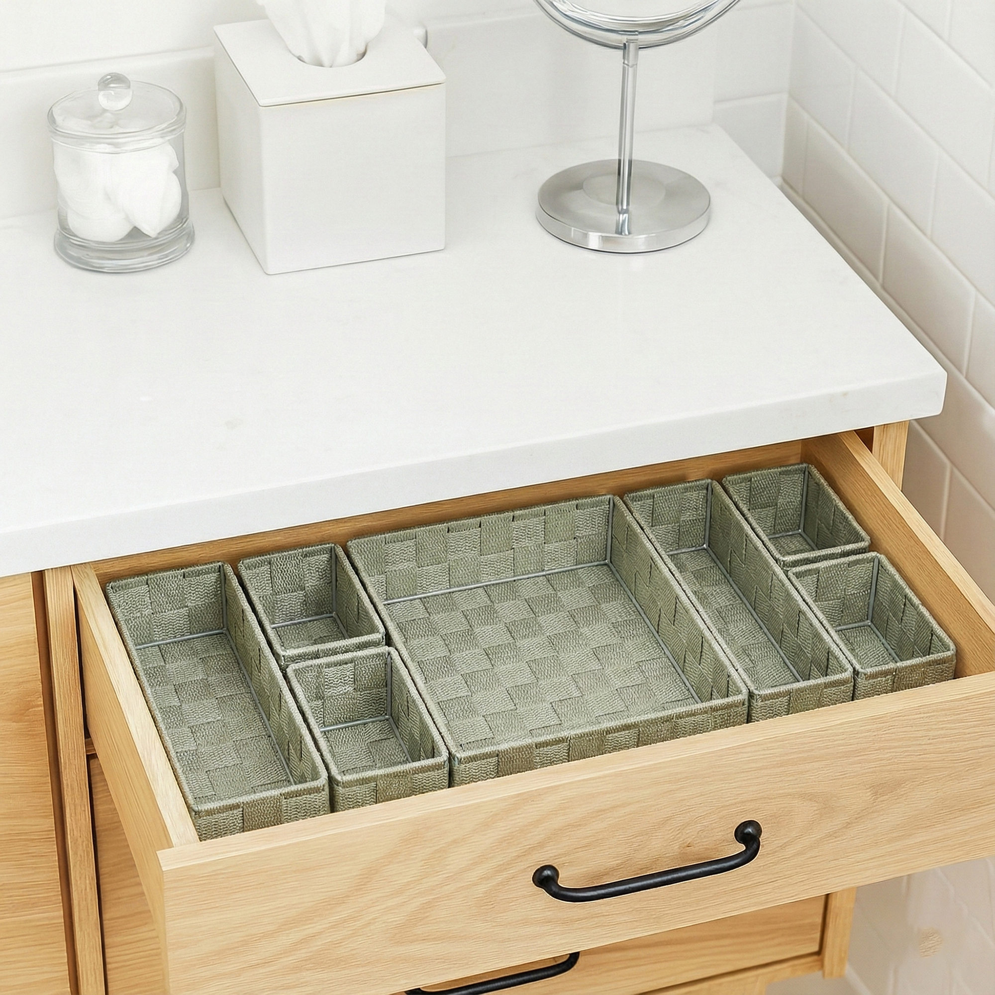 Seven-piece sage green braided drawer organizer bins arranged empty in an open wooden bathroom vanity drawer.