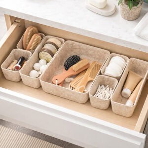 Beige felt drawer organizer set filled with beauty items including brushes, cotton pads, q-tips, and skincare products in an open bathroom drawer.