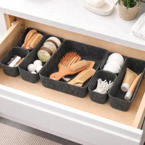 Dark gray felt drawer organizer set filled with beauty essentials including hairbrushes, cotton pads, q-tips, and skincare products in an open bathroom drawer.