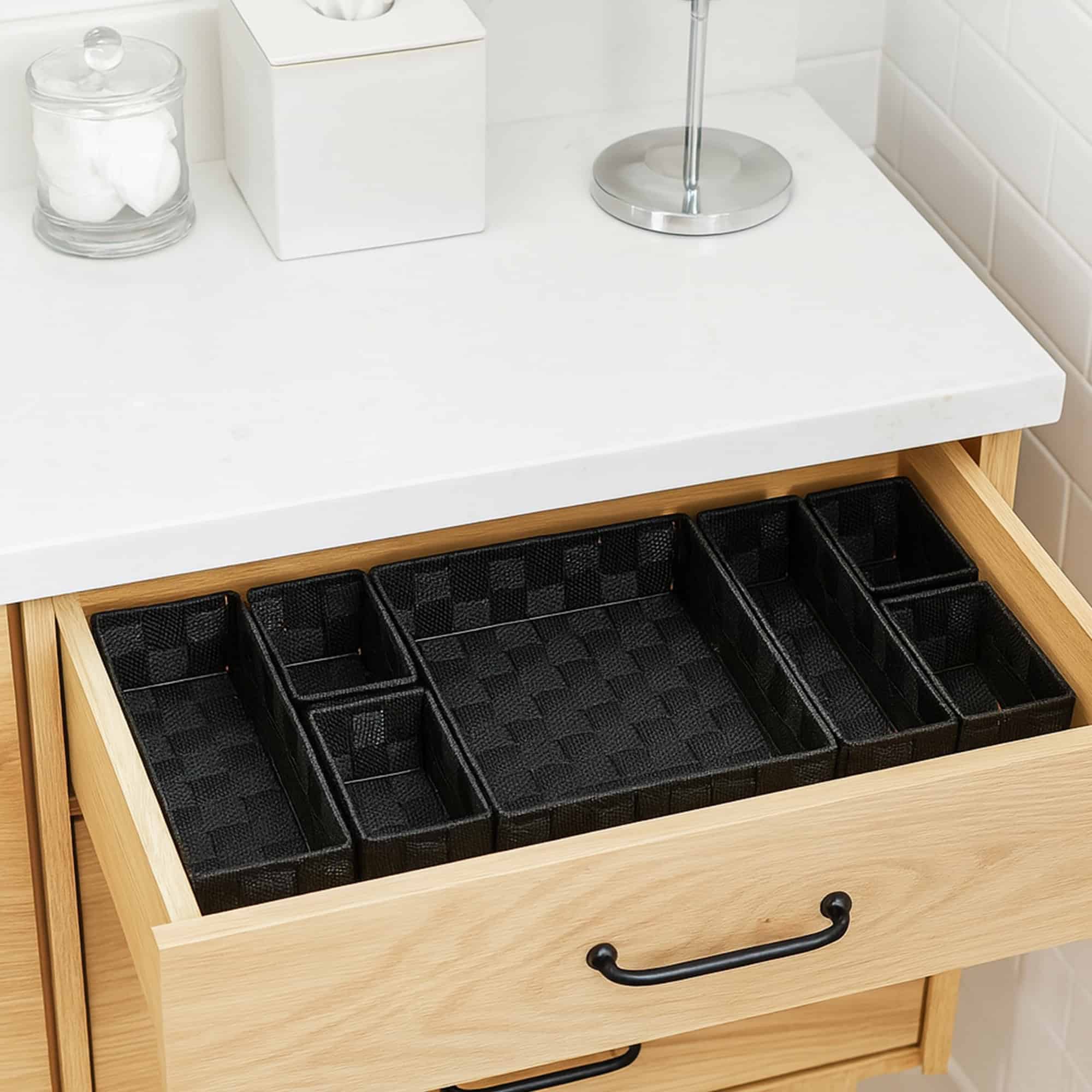 Seven-piece black braided drawer organizer bins arranged empty in an open wooden bathroom vanity drawer.