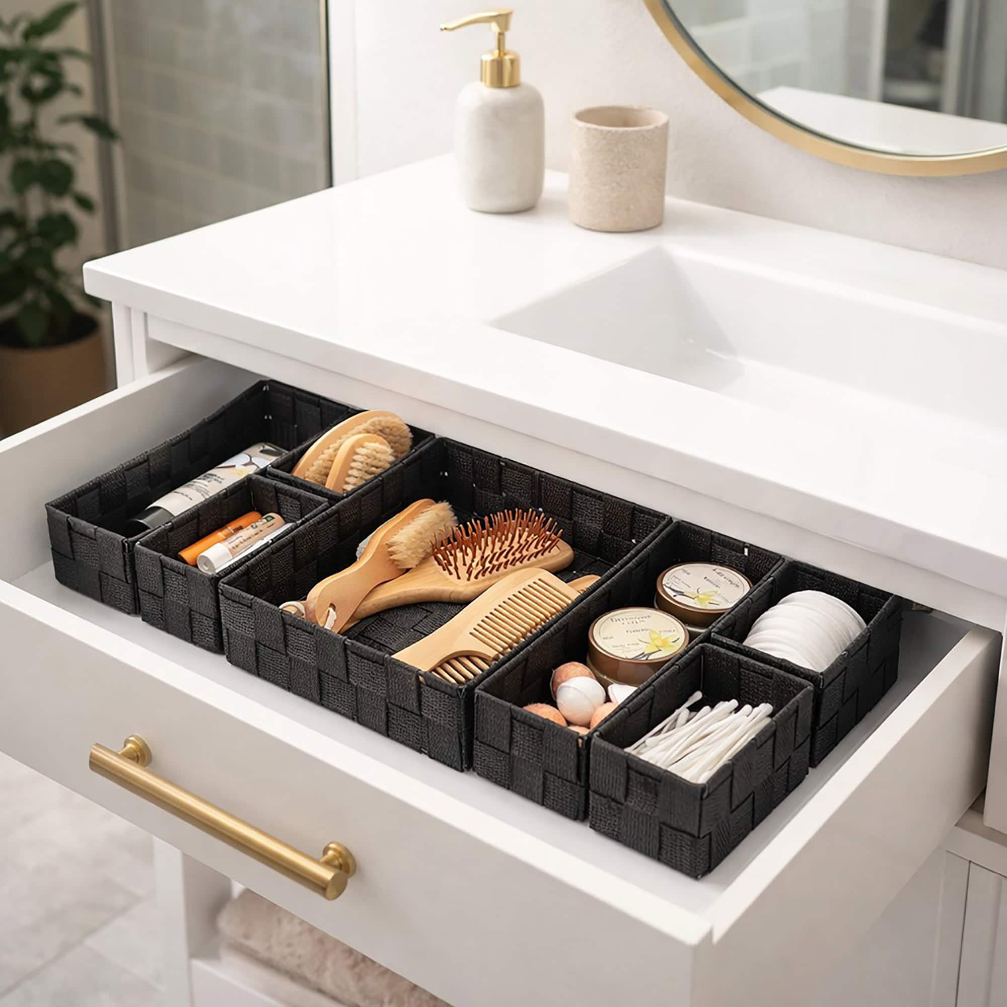 Black braided drawer organizer set filled with beauty essentials including hairbrushes, a comb, cotton pads, q-tips, and skincare products in an open white bathroom vanity drawer.