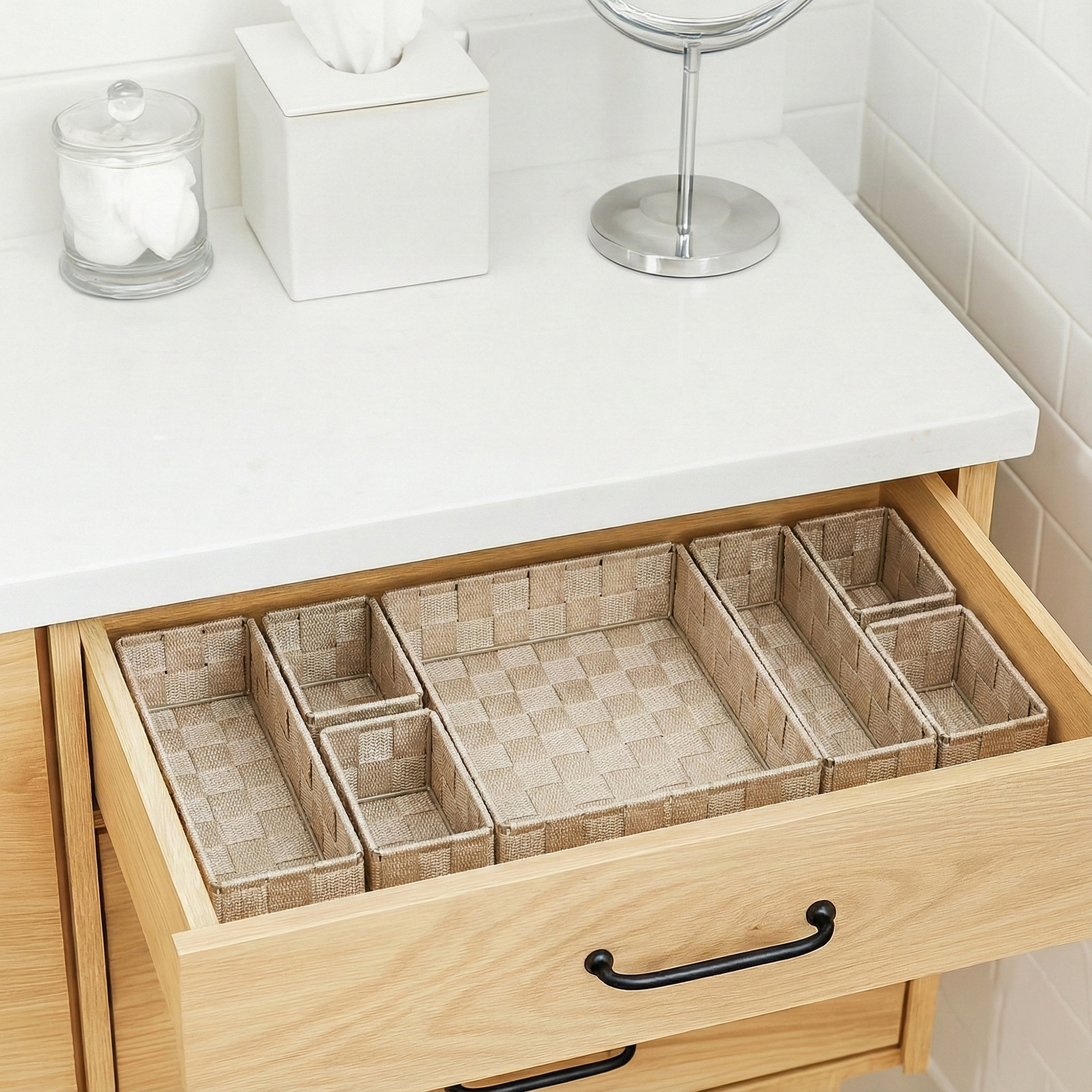 Seven-piece beige braided drawer organizer bins arranged empty in an open wooden bathroom vanity drawer.