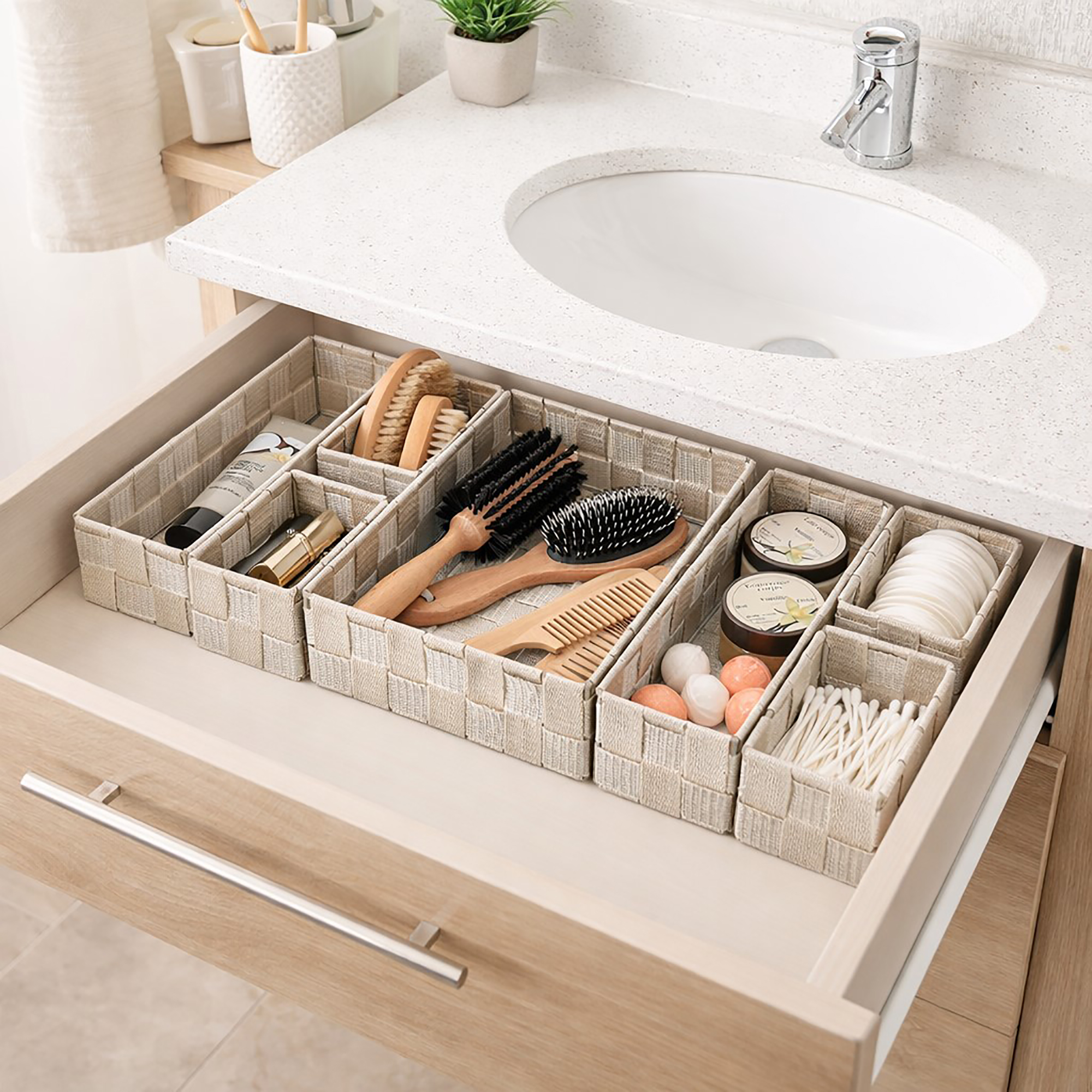 Beige braided drawer organizer set filled with beauty essentials including hairbrushes, a comb, cotton pads, q-tips, and skincare products in an open bathroom vanity drawer.