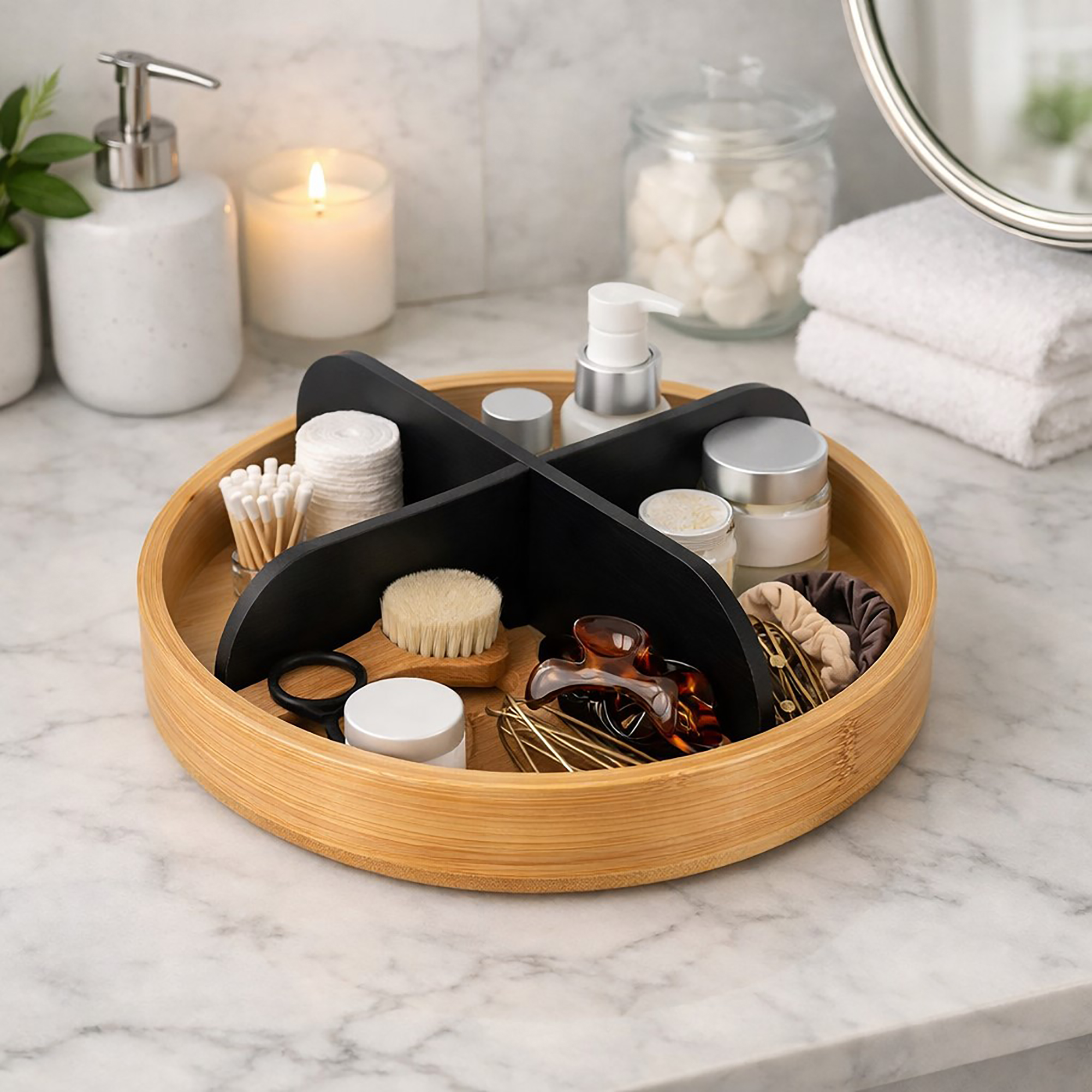 Round rotating bamboo tray with four black dividers, filled with cotton pads, q-tips, a face brush, hair clips, scrunchies, and skincare products on a marble bathroom countertop.