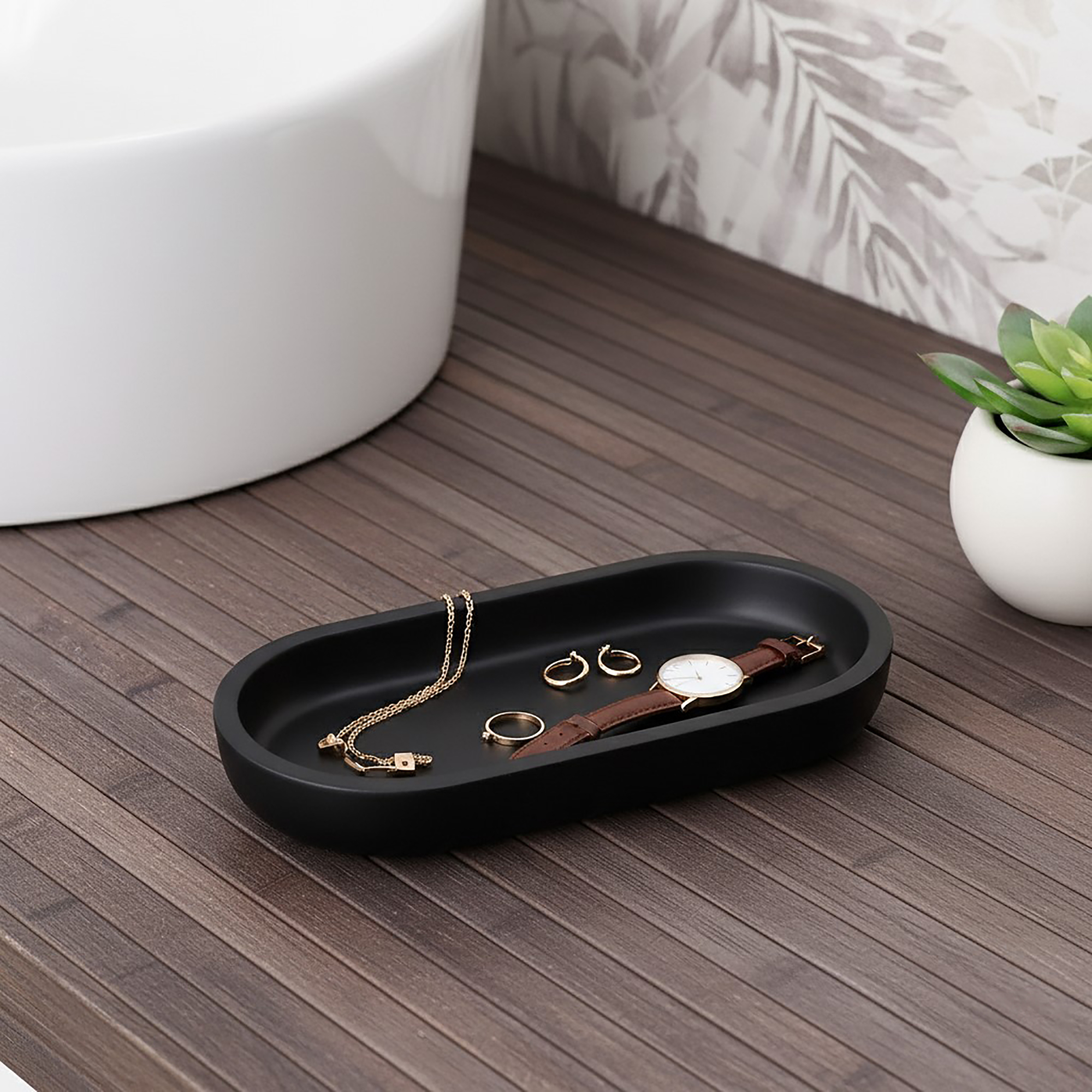 Black oval tray holding jewelry on bathroom counter
