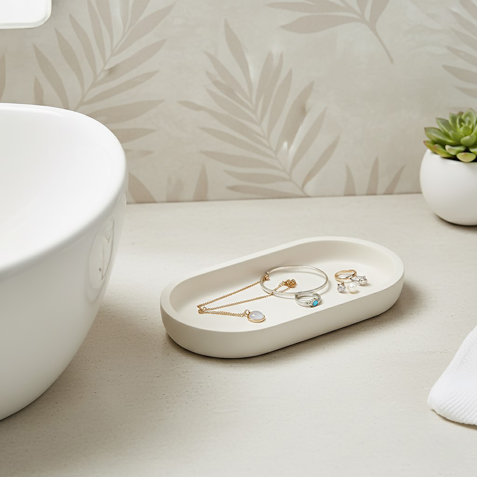 Beige oval tray holding jewelry on bathroom counter