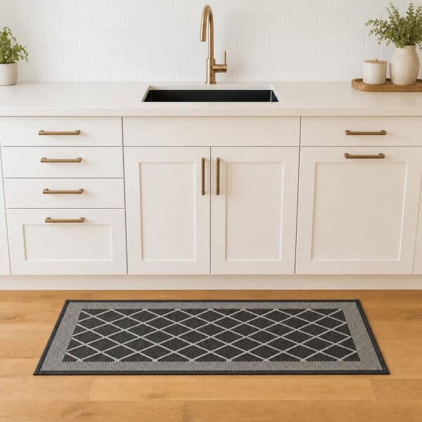 2- Charcoal gray diamond trellis kitchen runner with cream border on wood floor in front of a white sink