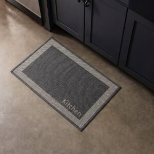 9- Charcoal kitchen mat with cream border and woven Kitchen word on concrete floor beside dark cabinets