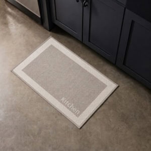 9- Taupe kitchen mat with cream border and woven Kitchen word on concrete floor beside dark cabinets