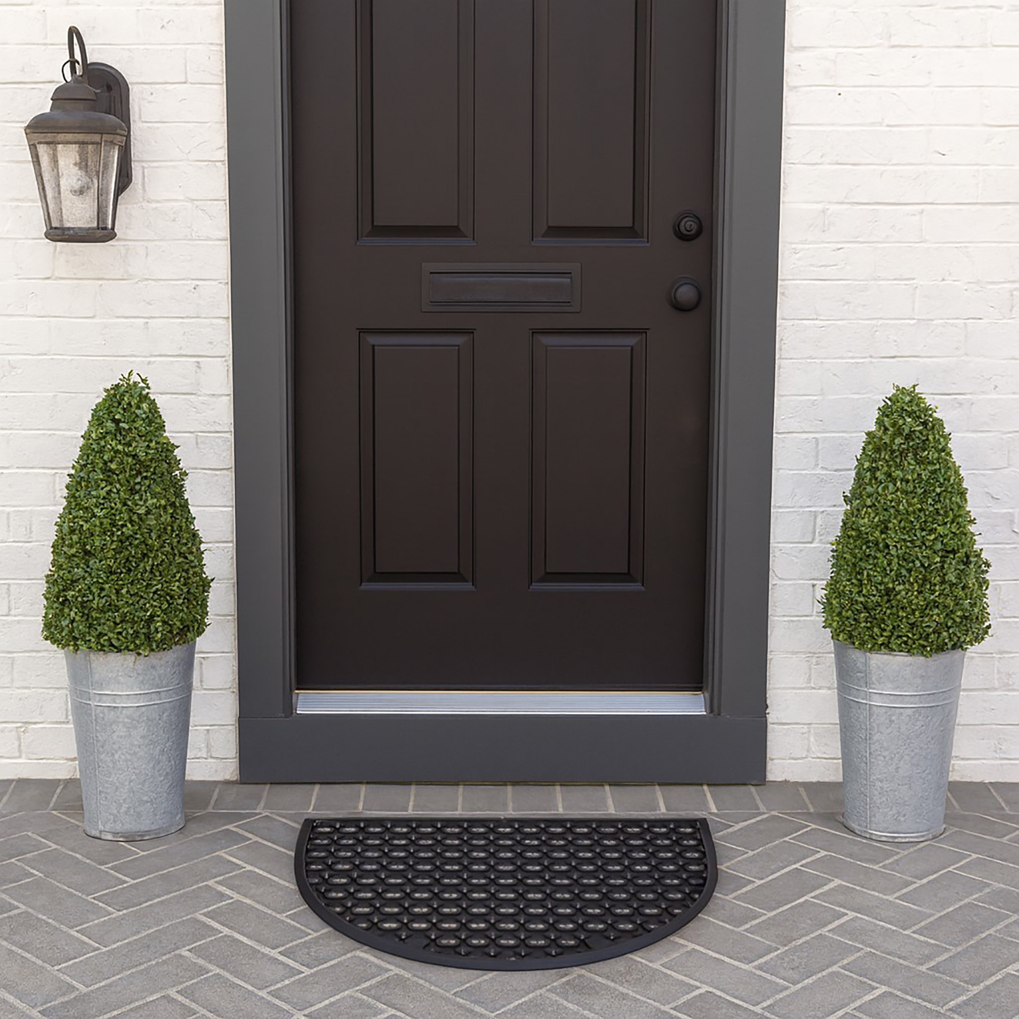 Black half-moon rubber doormat at front door with potted plants
