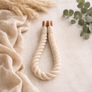 An ecru twisted cotton rope curtain tieback with wooden magnetic ends, laid flat on a white surface